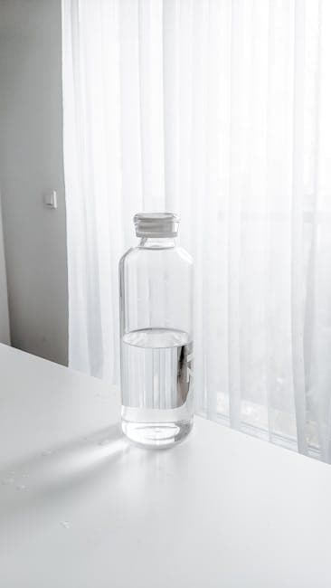 Clear water bottle on a white desk with sheer curtains background, minimalist setting.
