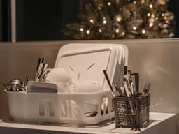 A dish rack with dishes and utensils beside a Christmas tree, creating a warm festive kitchen atmosphere.