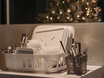 A dish rack with dishes and utensils beside a Christmas tree, creating a warm festive kitchen atmosphere.