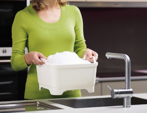 Égouttoir à vaisselle en plastique robuste, blanc et vert, avec système d’évacuation de l’eau de rinçage et poignées latérales. Il se pose dans ou à côté de l’évier. Joseph Joseph
